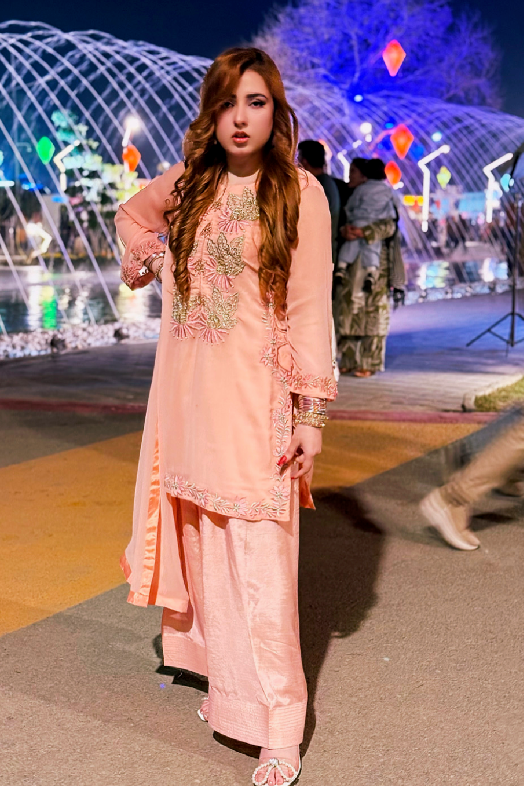 Woman in a peach traditional outfit with embroidery standing in front of a colorful light display.