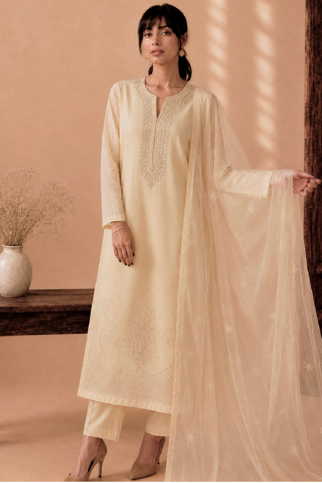 Woman wearing a light beige kurta with a dupatta in a warm-toned room.