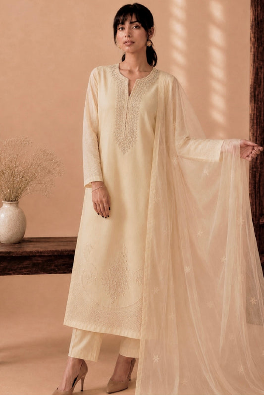 Woman wearing a light beige kurta with a dupatta in a warm-toned room.