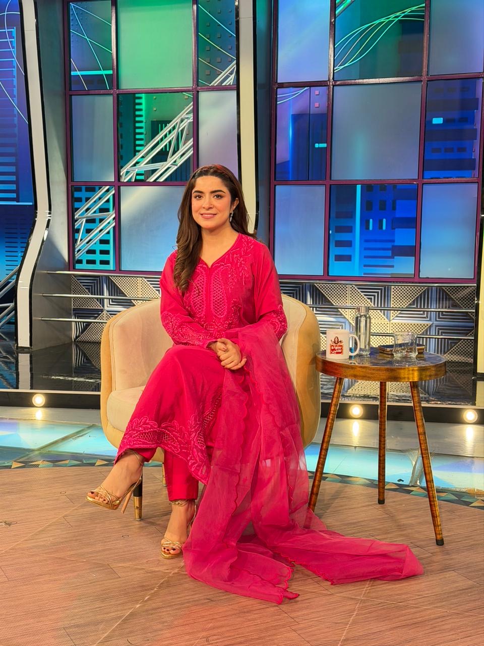 Woman in a bright pink traditional outfit sitting on a set with colorful geometric background