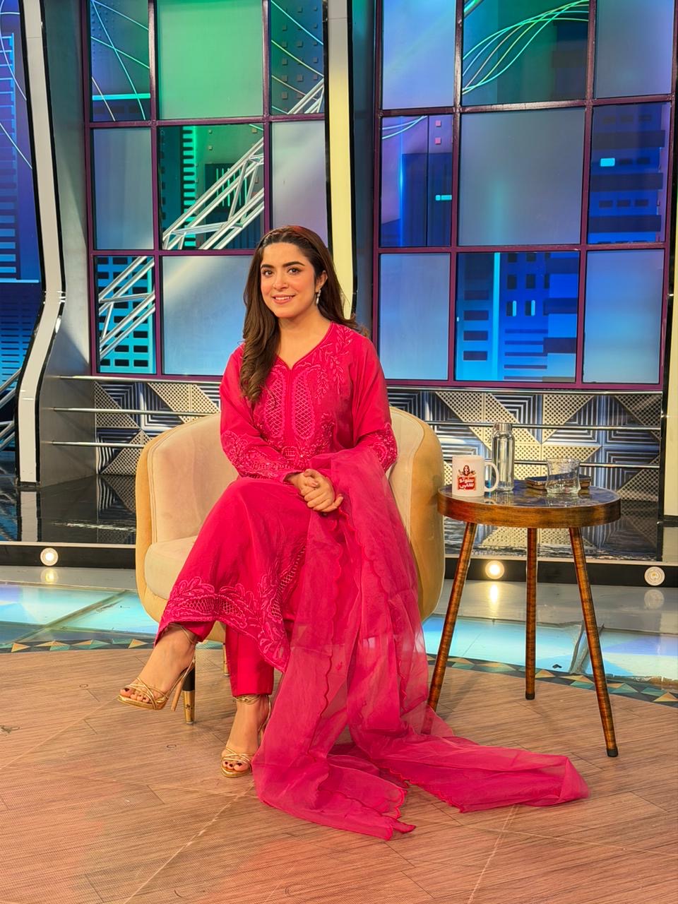 Woman in a bright pink traditional outfit sitting on a set with a modern design.