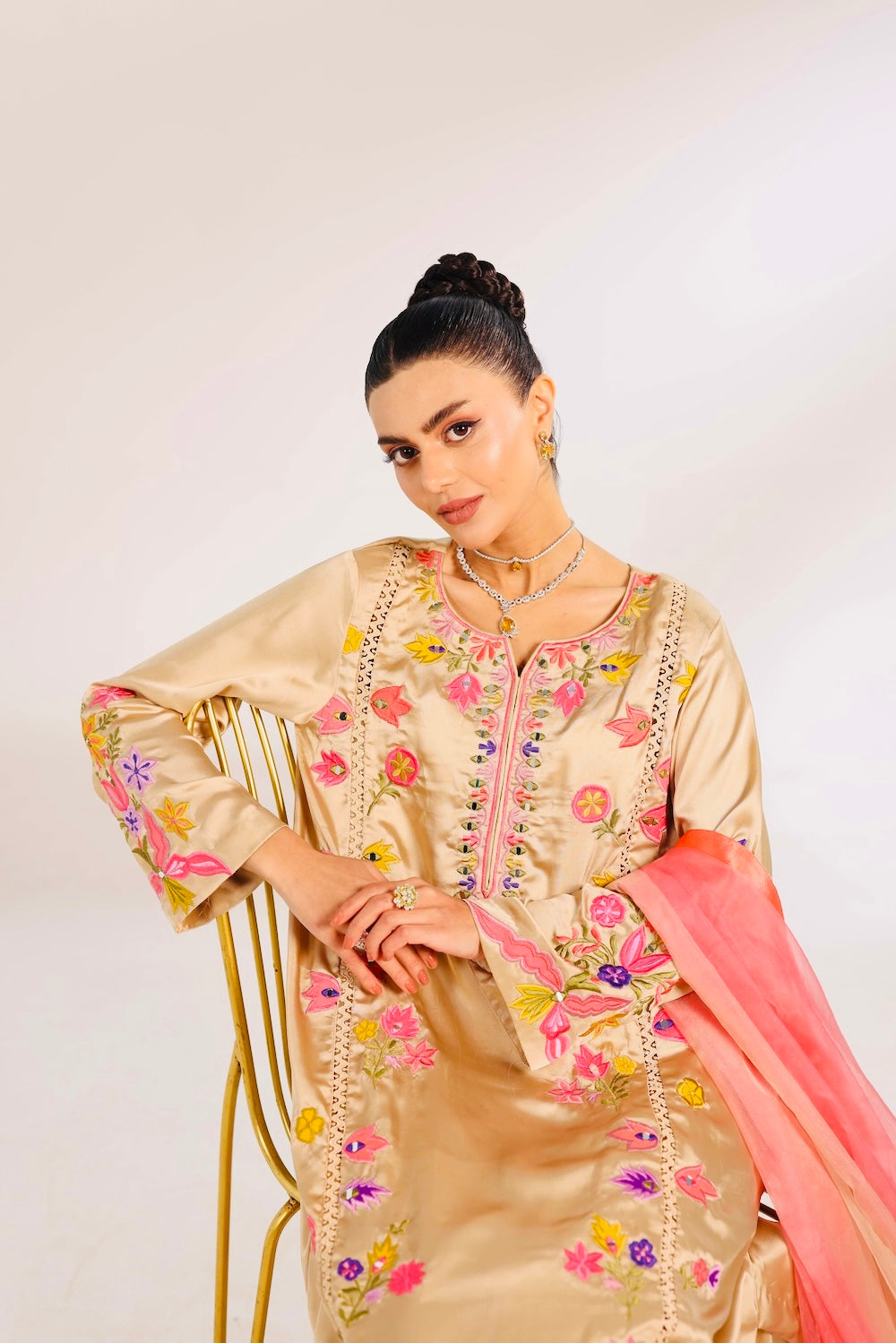 Woman wearing a traditional embroidered outfit with a pink dupatta on a white background