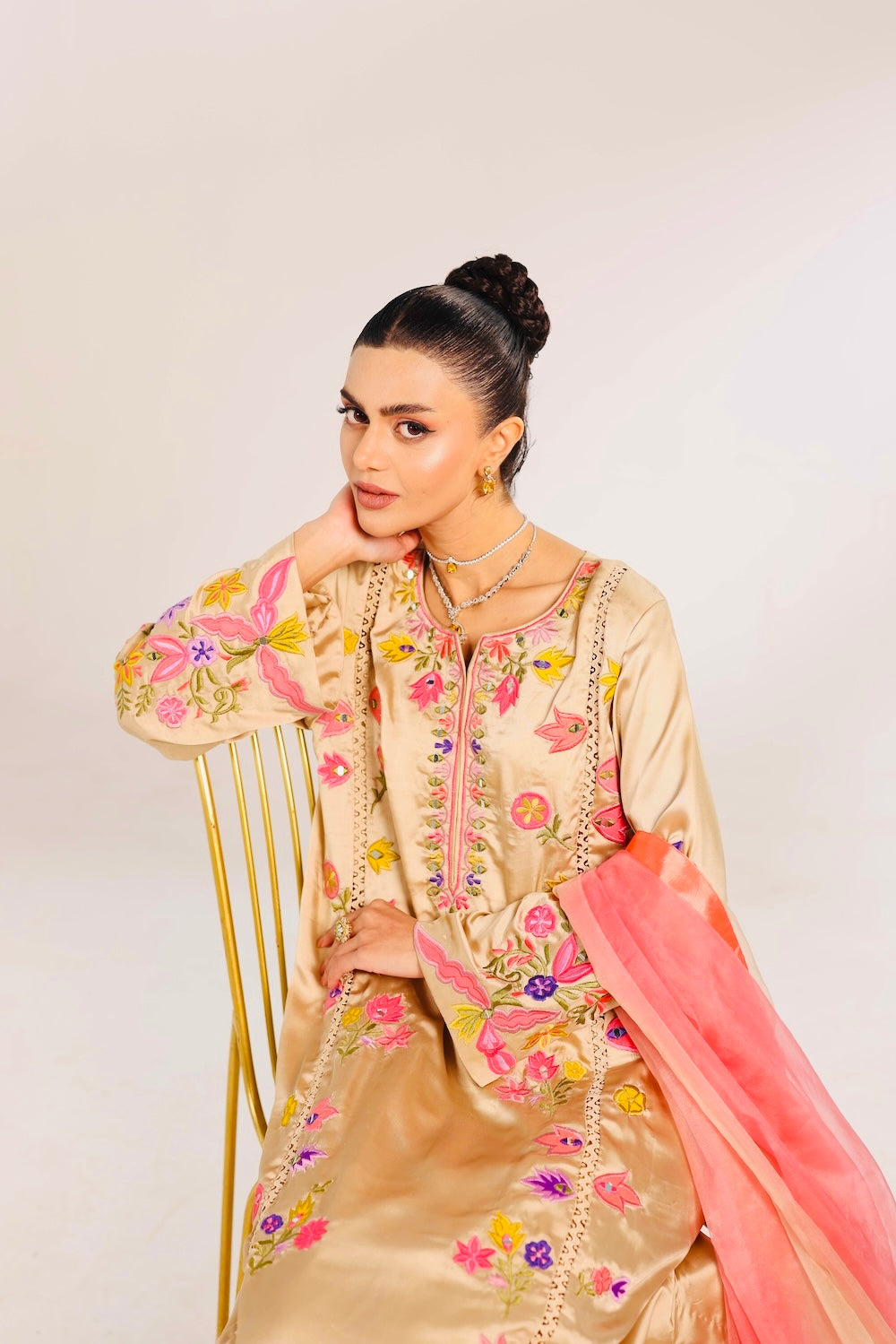 Woman wearing a traditional embroidered outfit with a pink dupatta on a white background