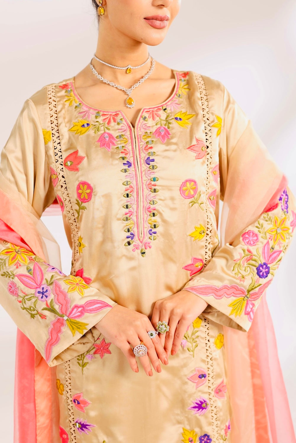 Beige embroidered traditional outfit with colorful details on a plain background