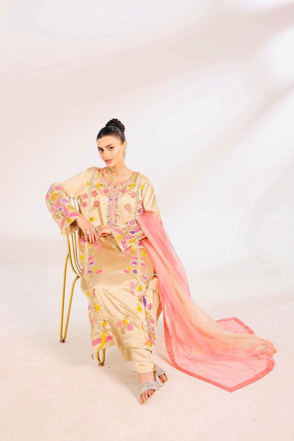 Woman in a traditional Desi Pakistani outfit with floral patterns and a pink dupatta on a white background