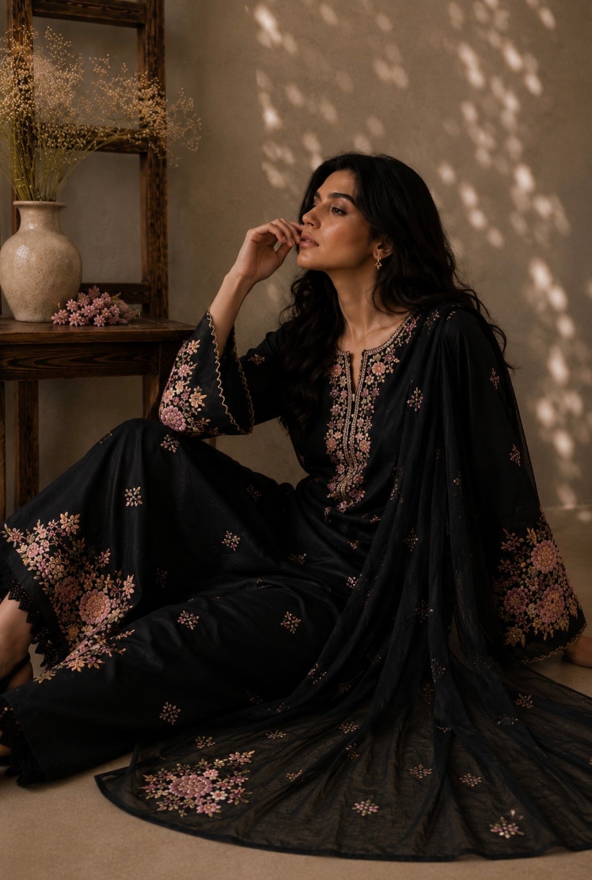 Woman in a black embroidered outfit sitting indoors with soft lighting