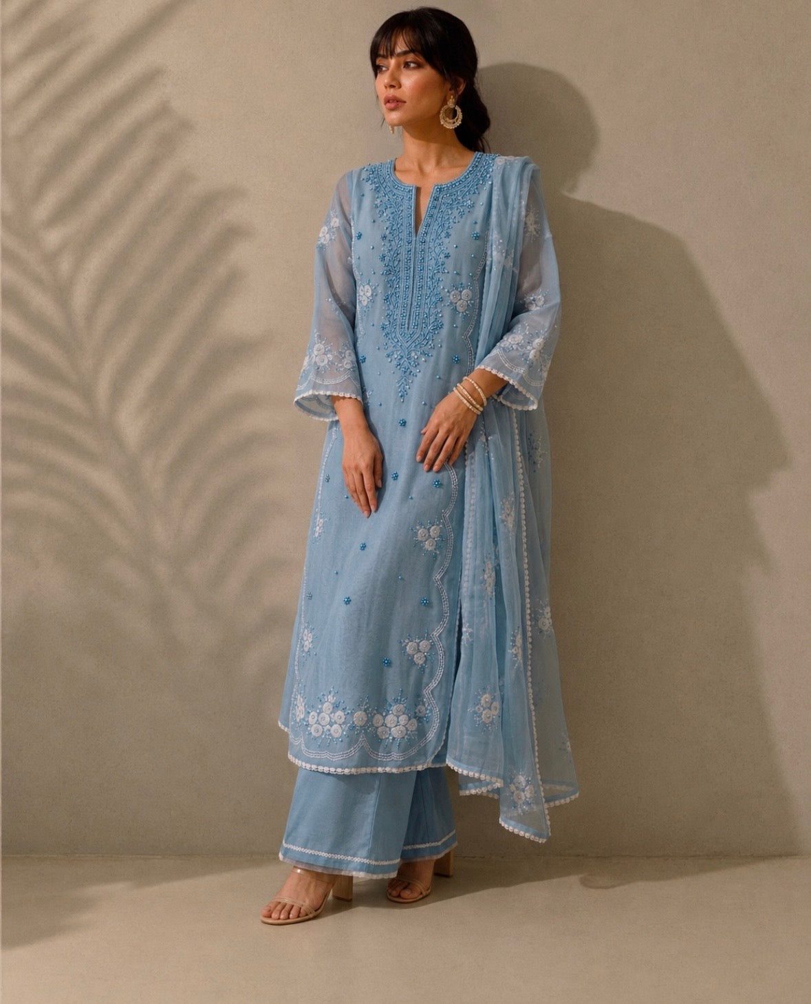 Woman wearing a light blue embroidered traditional outfit against a neutral background