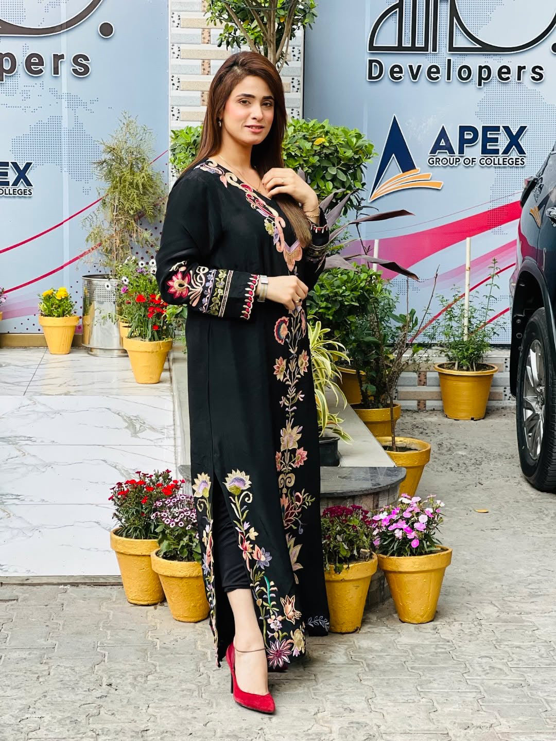 Woman in a black embroidered dress standing in front of promotional boards for Apex Group of Colleges.
