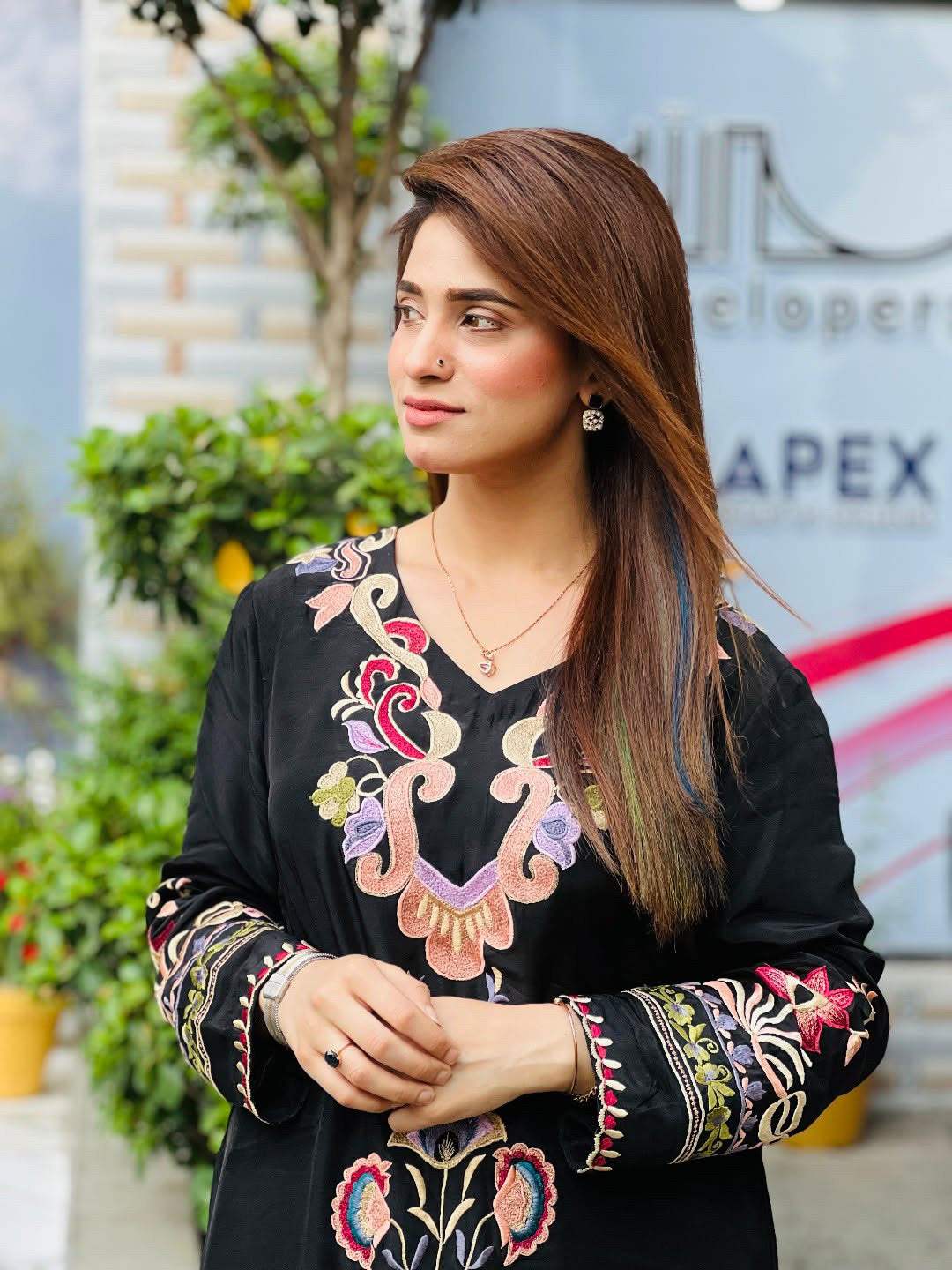 Woman wearing a black embroidered top with colorful patterns in an outdoor setting.