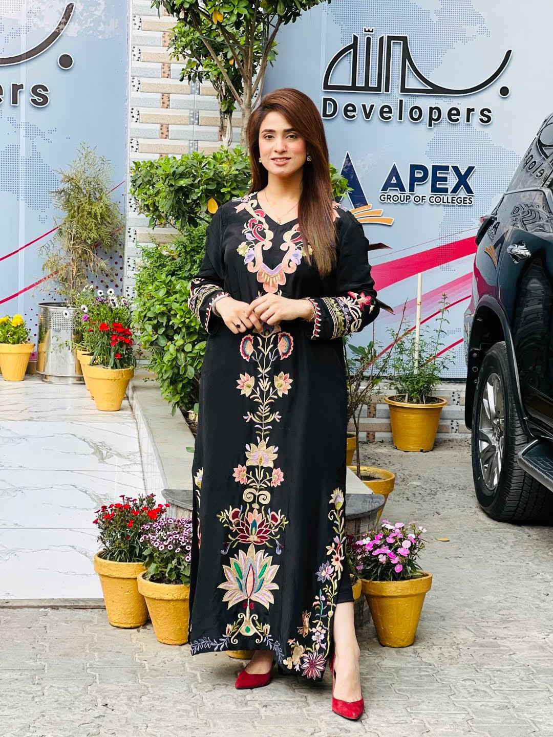 Woman in a black embroidered dress by farah. K standing in front of a building 