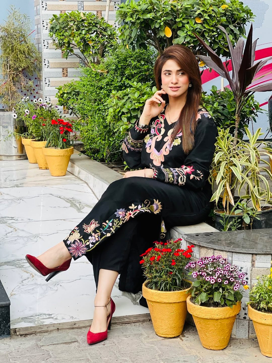 Woman sitting on steps surrounded by potted plants wearing black kaftan 
