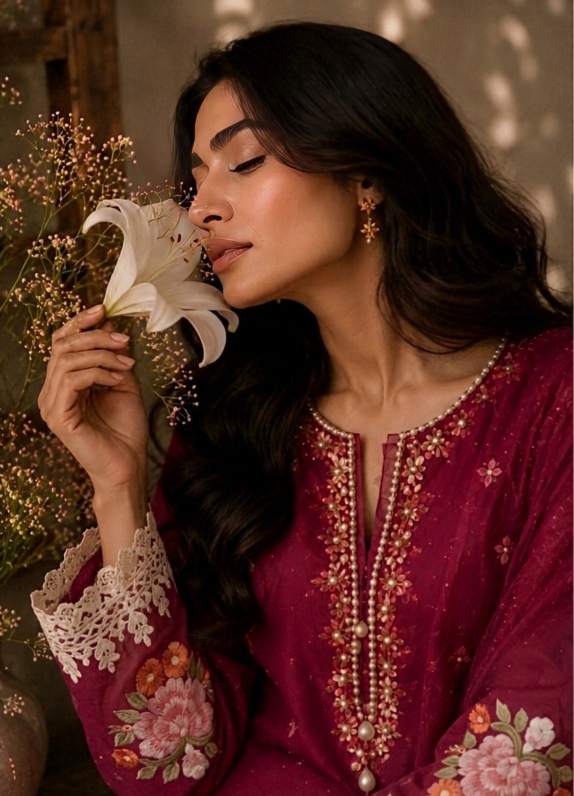 Woman holding a white flower, wearing a red embroidered traditional outfit with floral patterns.