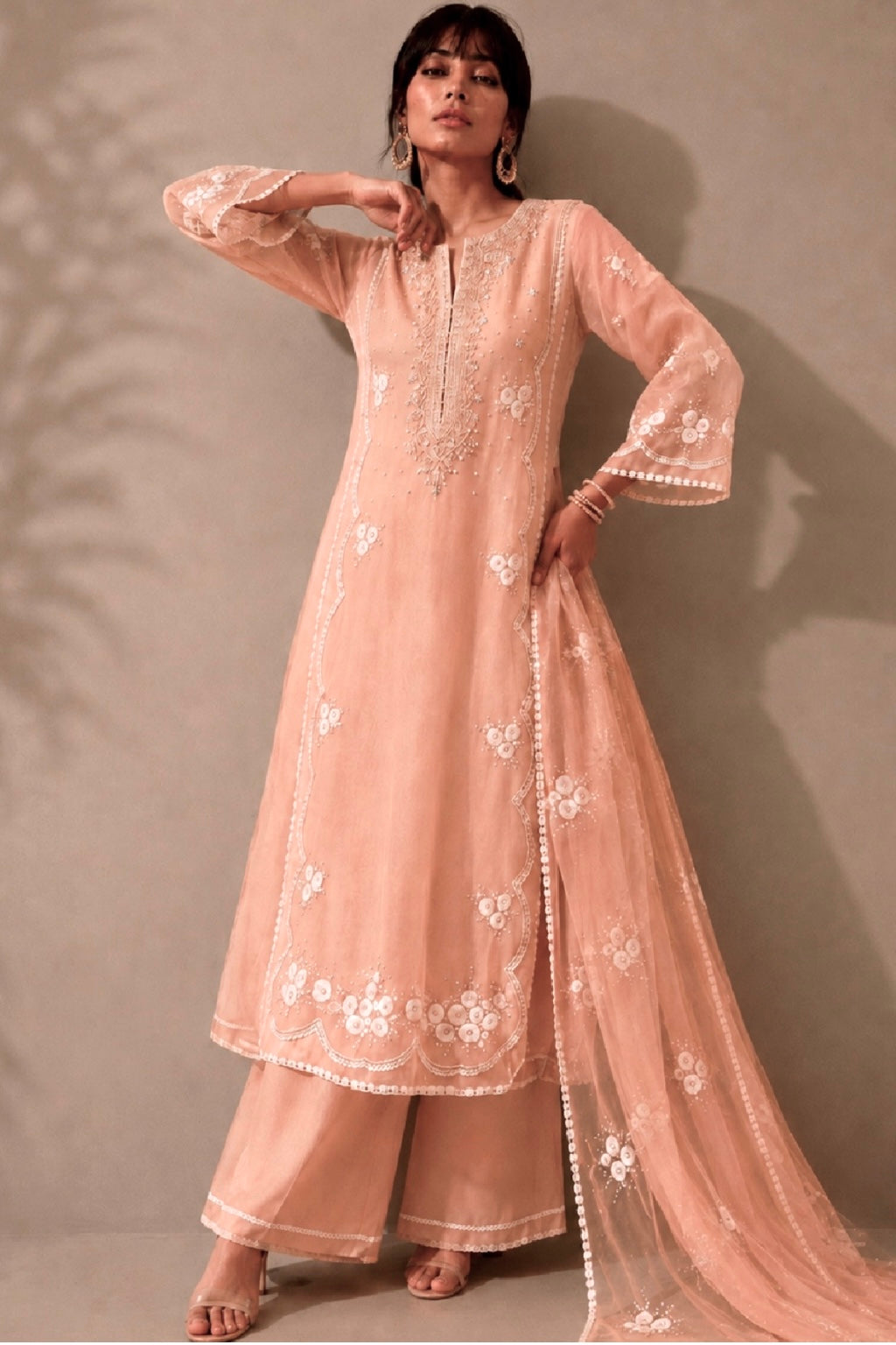 Woman wearing a peach embroidered traditional outfit against a neutral background