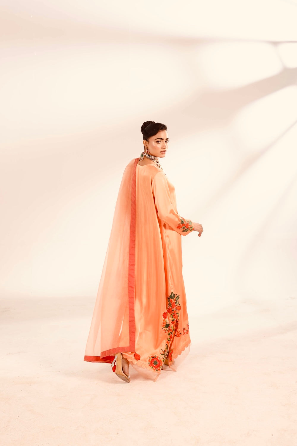 Woman wearing a peach-colored traditional outfit with a floral design on a white background