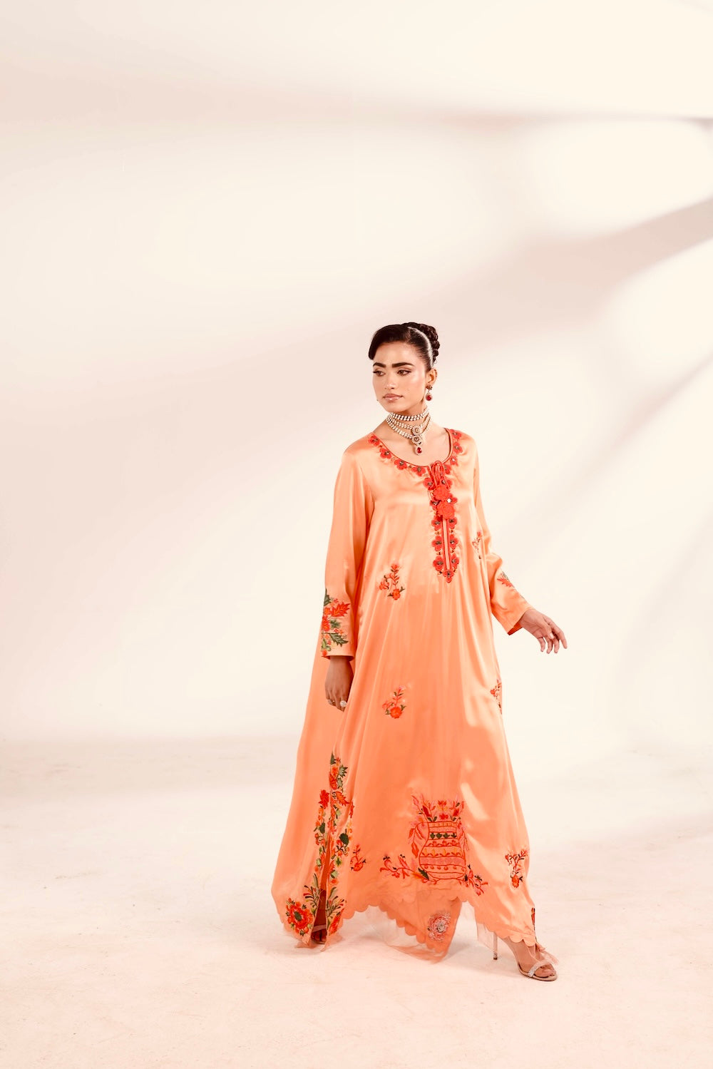 Woman wearing a peach-colored embroidered outfit on a white background