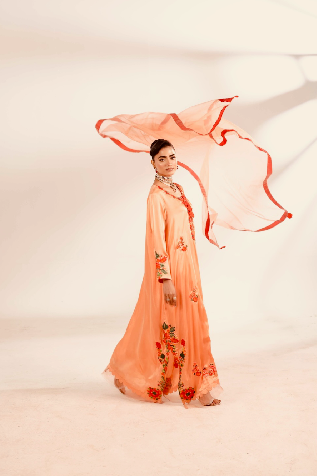 Woman in a peach-colored traditional outfit with a flowing scarf against a light background