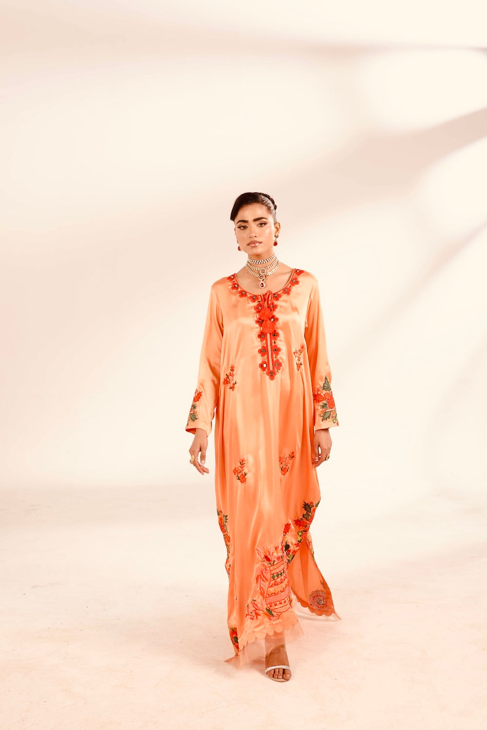 Woman wearing a peach-colored dress with floral embroidery on a white background