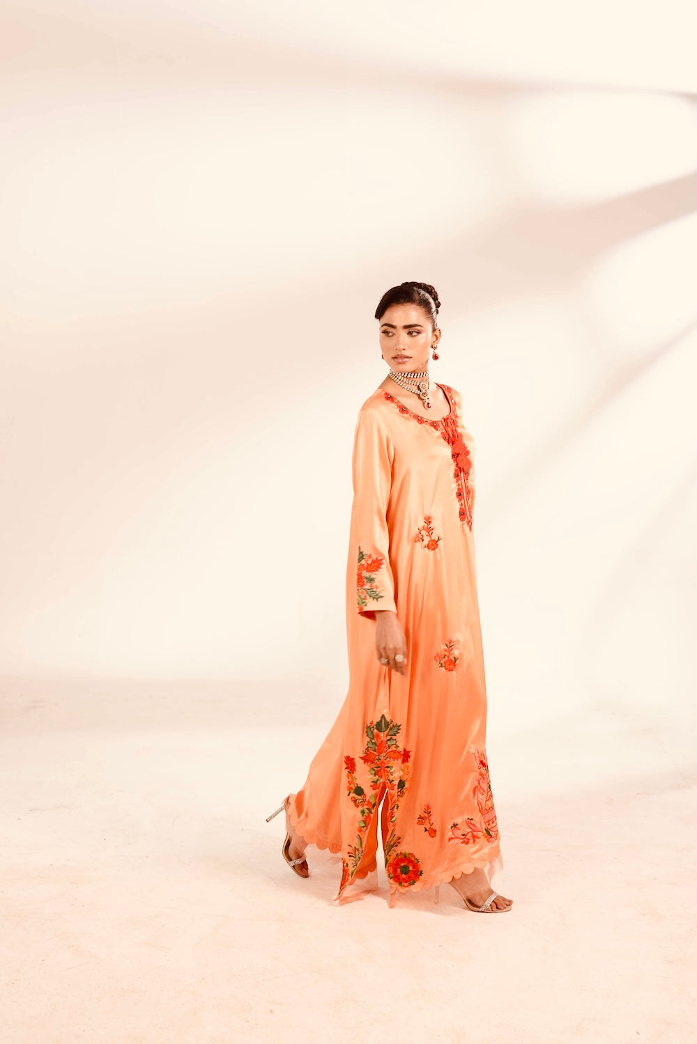 Woman wearing a peach-colored dress with floral embroidery on a white background